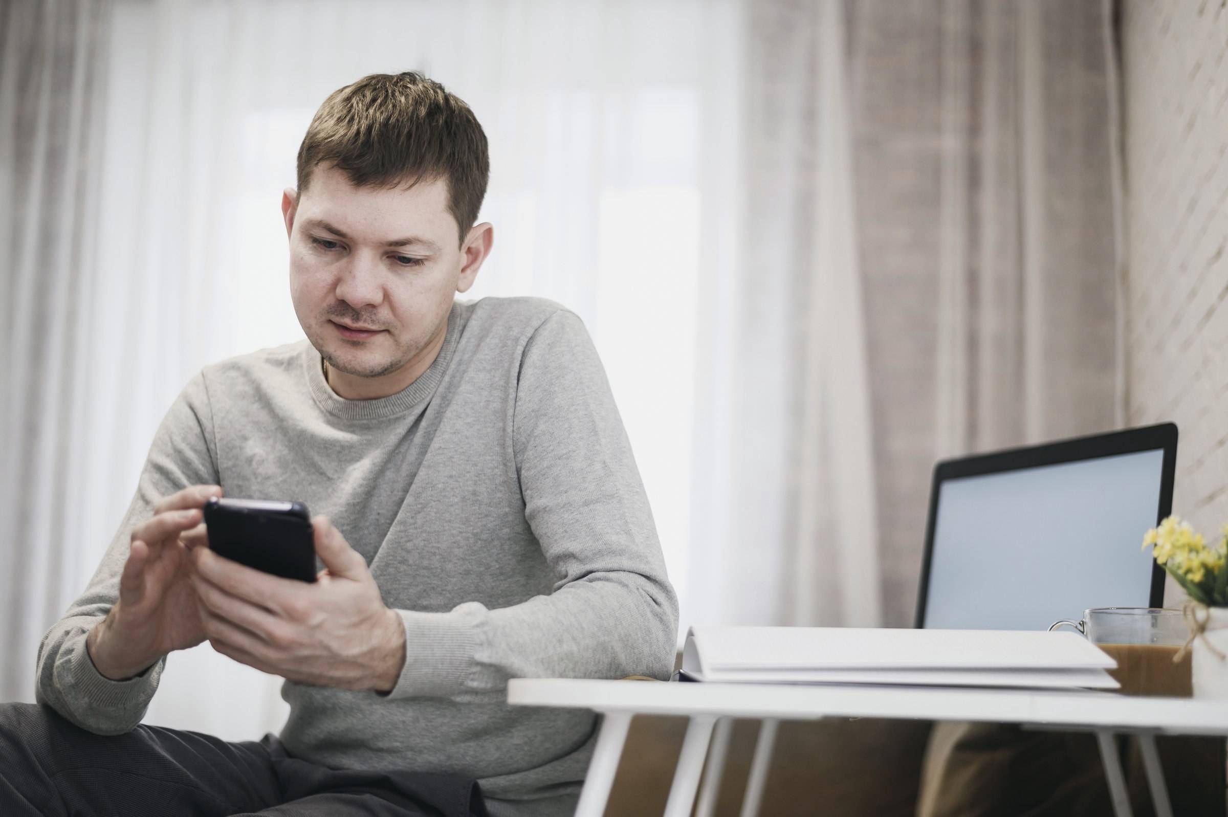 Mann sitzt zu Hause und tippt auf seinem Smartphone